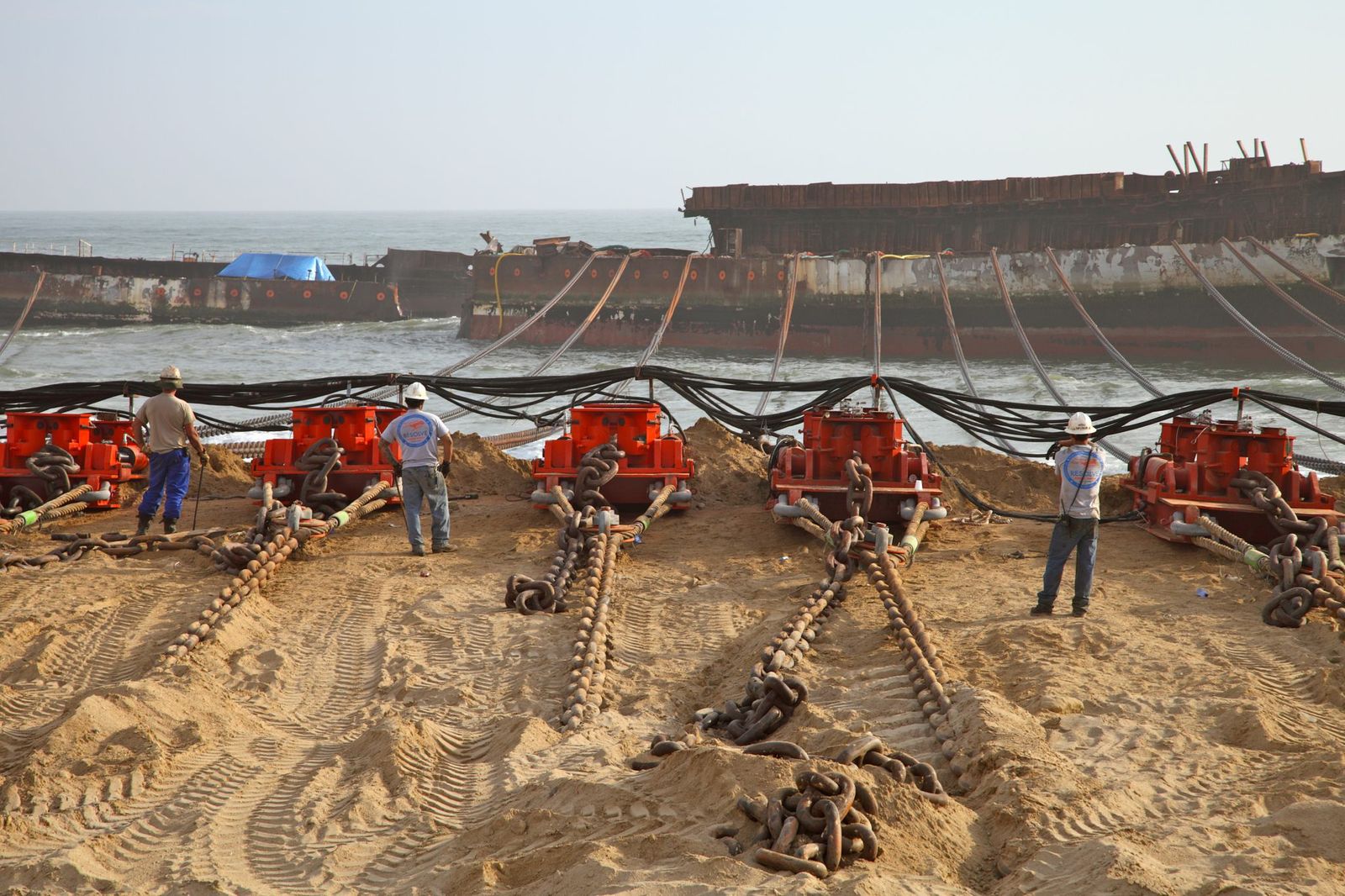 Workers supervise the attachment of chains to a failing ship.